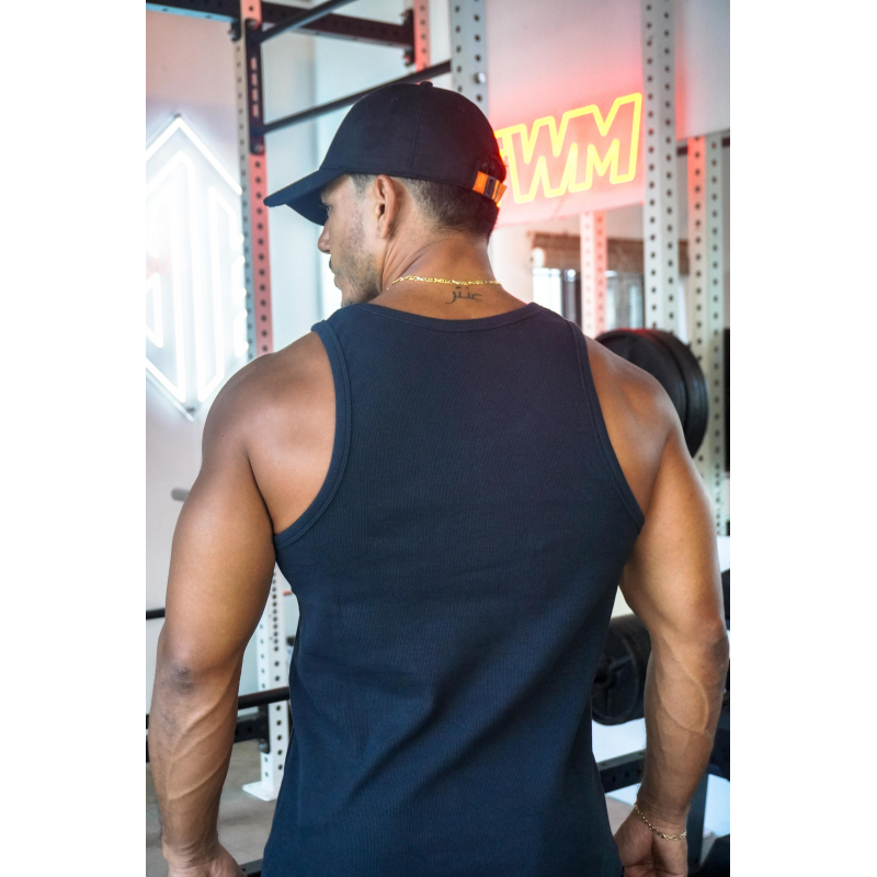 Homme vu de dos portant un débardeur noir ESSENTIAL dans une salle de musculation, casquette noire et collier doré, portant une