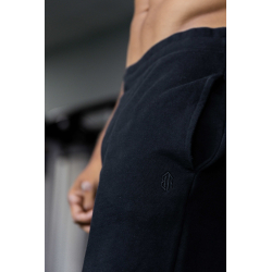 Homme sportif portant un pantalon de jogging noir, vue rapprochée sur la taille et une couture, logo discret sur le tissu noir.