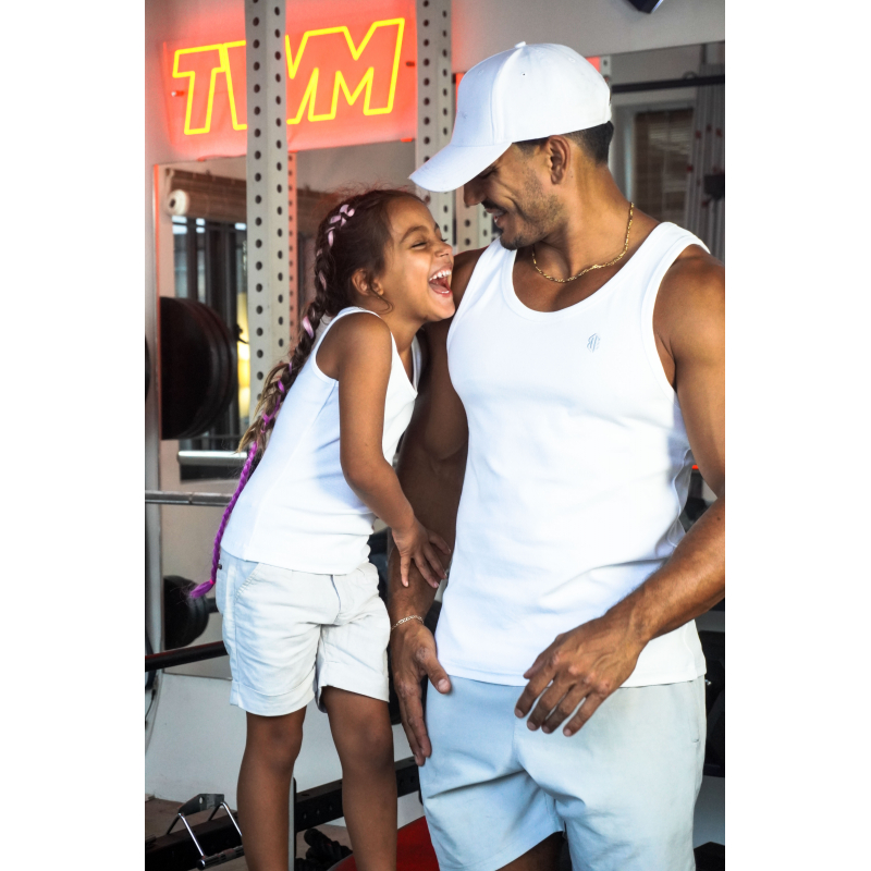 Deux personnes dans une salle de sport: un homme en débardeur blanc et casquette blanche souriant avec une jeune fille qui rit, les deux portant des tenues sportives blanches et bleues.