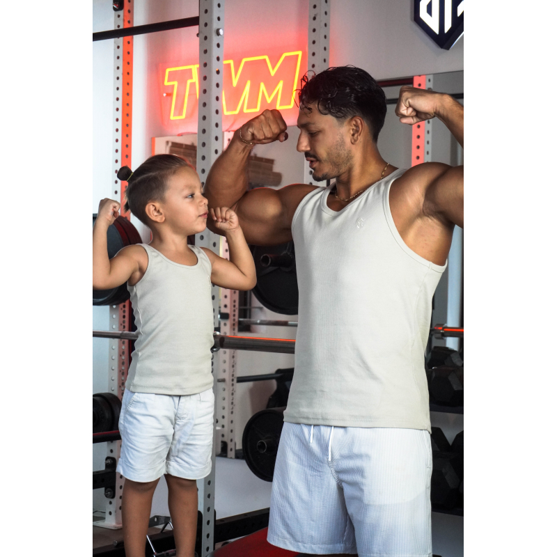 Deux personnes en salle de sport: un homme adulte musclé en débardeur gris et un jeune enfant blanc en débardeur et short blanc, se regardant et montrant leurs biceps en flexion près d’un rack de poids. Deux personnes en salle de sport: un homme adulte musclé en débardeur gris et un jeune enfant blanc en débardeur et short blanc, se regardant et montrant leurs biceps en flexion près d’un rack de poids.