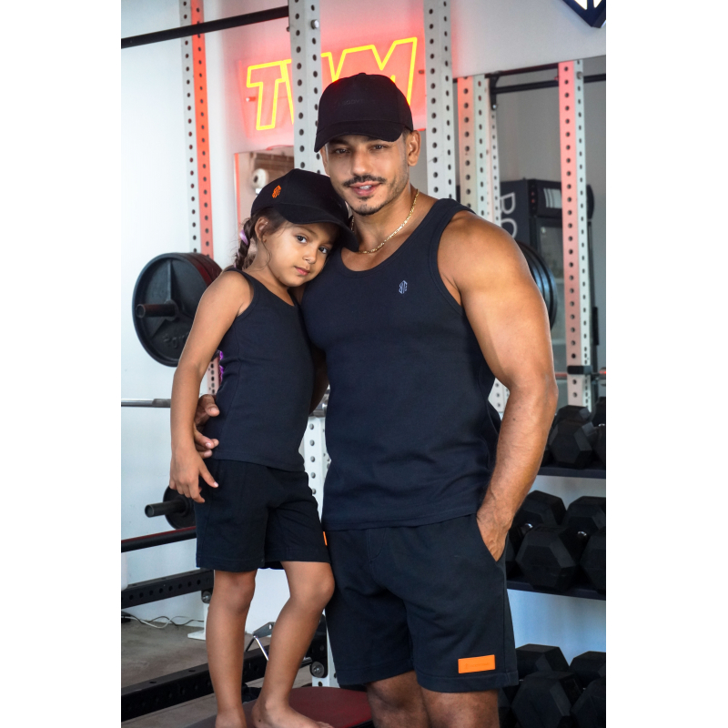 Homme et jeune fille en tenue de sport noire dans une salle de musculation, posant ensemble près d’un rack de poids, ambiance studio.