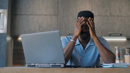 Homme fatigué devant un ordinateur portable au travail, tête dans les mains, signes de stress au travail.